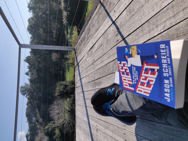 A picture of me resting a book called Press Reset on my legs while looking at the horizon.